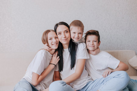 A happy mom sits at home on the couch in the arms of her children. Understanding supporting the trust of an idyllic conceptの写真素材