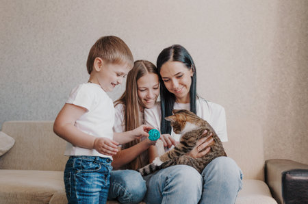 beautiful happy family mom and two kids playing with a cat sitting on the couch.の写真素材