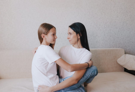 mom and daughter are sitting on the couch with their arms around each other and looking at each otherの写真素材