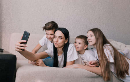 a beautiful mother with her children takes a selfie on her phone while lying on the couch. happy friendly familyの写真素材