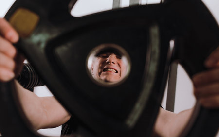 tense and full of pain, the face of a man lifting a weight in a fitness club. sports training healthy lifestyle.の写真素材