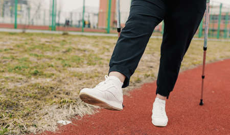 nordic walking. close-up of a woman's legs in white sneakers on a red treadmill. healthy lifestyle. morning exercise.の写真素材