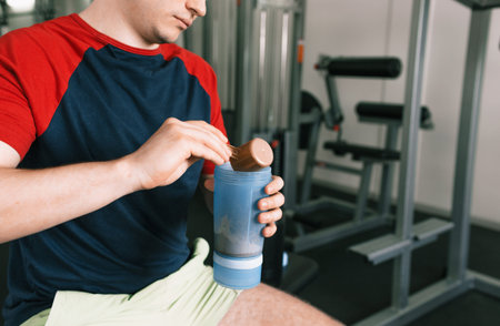a man pours protein into a shaker after a workout while sitting on a bench in the gym. sports nutritionの写真素材