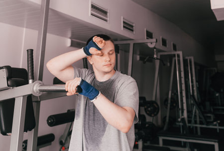 a portrait of a tired athlete in a wet T-shirt stands near the simulator. rest after an intense...