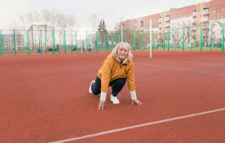 an elderly woman in a yellow jacket is doing sports exercises on a red treadmill. the stadium is a healthy lifestyle. retired people and sports. active old womanの写真素材