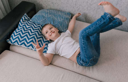 a happy little boy lies on the couch on his back looking up and smiling.の写真素材