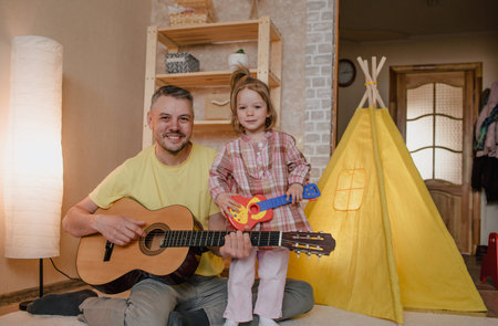 portrait of a happy father with a guitar in his hands and a little girl sitting on her father's lap....