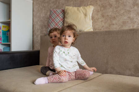 two small similar girls are sitting on the couchの写真素材