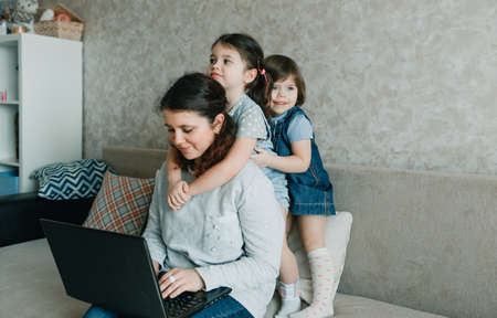 Happy mom working at home on the computer surrounded by small childrenの写真素材