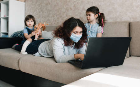 two little girls sit on their mother's back while working on the computer. remote work at homeの写真素材