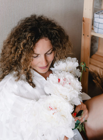 a large portrait of a woman in a white dress with curly hair holding a bouquet of white peonies in her hand.の写真素材