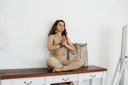 a young beautiful girl meditates sitting in a lotus position on a table. light backgroundの写真素材