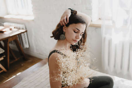 a beautiful young girl with a bouquet of white flowers is sitting on the bed with her eyes closed. women's happinessの写真素材