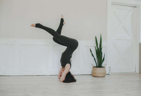 The girl does yoga. A young woman is practicing asanas at a large white wall. Upside down. healthy lifestyleの写真素材