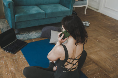 A young woman does sports at home. A cheerful athlete with black hair, and studies from a laptop. healthy lifestyleの写真素材