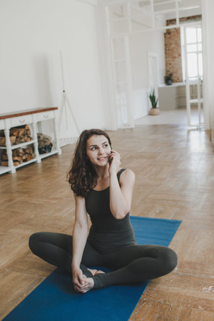 a girl rests after a workout and talks on the phone while sitting on a sports mat. healthy lifestyle...