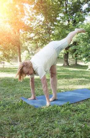A mature woman in a T-shirt and shorts does fitness exercises outdoors. he makes bends by lifting his leg high. healthy lifestyleの写真素材