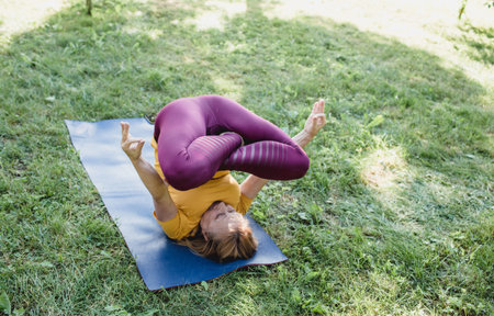 an old woman does yoga in the park on the grass performs a complex exercise. healthy lifestyle