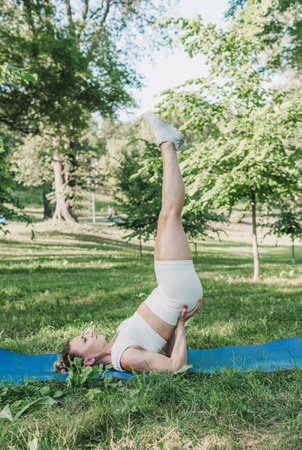 the girl performs complex yoga exercises in the park on a gym mat.の写真素材