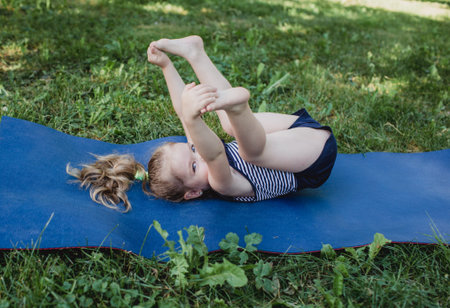 a little girl does yoga lying on a sports mat in the park. a healthy lifestyle is a childish habit.