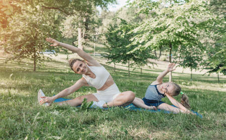 Mother and daughter do yoga exercises on the grass in the park during the day. healthy lifestyleの写真素材