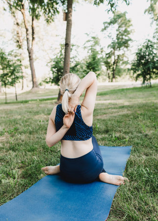 A woman practicing yoga asanas outdoors. A young attractive slender fitness girl in a bodysuit