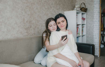 mother and daughter hugging together using the phone, a young woman and daughter looking at the smartphone screen,の写真素材