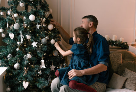 Christmas Eve, dad and daughter decorate the Christmas tree at home.