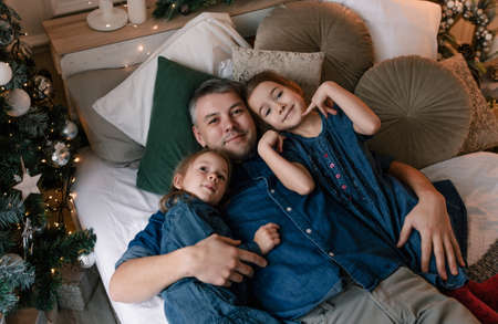 happy father lies in bed hugging two little daughters on Christmas eveの写真素材