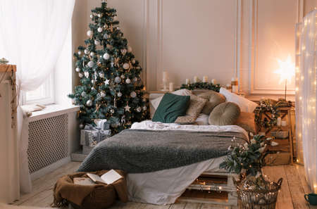 decorated room for winter holidays, a Christmas tree and a white bed next to itの写真素材