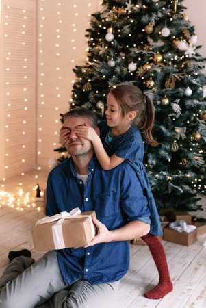 Cute little girl closes daddy's eyes daddy holds a gift box, New Year's interior.