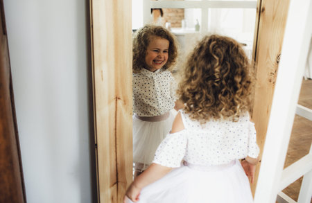 a little curly-haired girl looks at herself in the mirror and laughsの写真素材