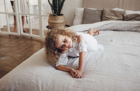 a little girl with curly hair is lying in the middle of a large bedの写真素材