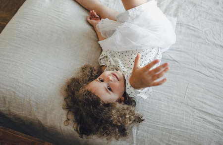 a little girl with curly hair is lying in the middle of a large bedの写真素材