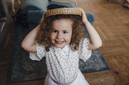 beautiful little curly-haired girl with a wicker basket on her headの写真素材