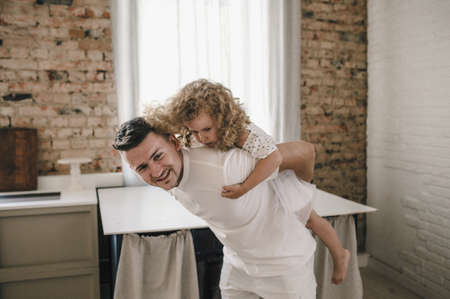 Happy positive cheerful dad is playing with his little charming daughter at home. The man circles and throws the girl up.の写真素材
