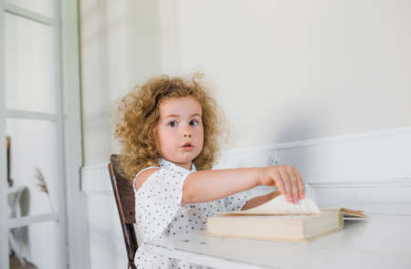 a little girl is sitting at a table in front of an open book. home schoolingの写真素材