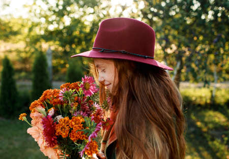 portrait of a red-haired teenage girl in a red hat holding a bouquet of flowersの写真素材