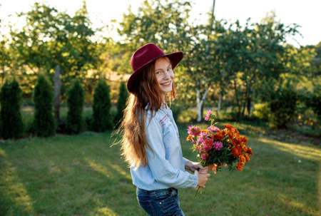 a red-haired teenage girl in a red hat dances on the lawn with a bouquet of flowersの写真素材
