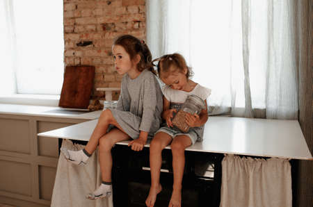two little girls are sitting on a large kitchen table, holding a glass jar of buckwheat in their hands.の写真素材