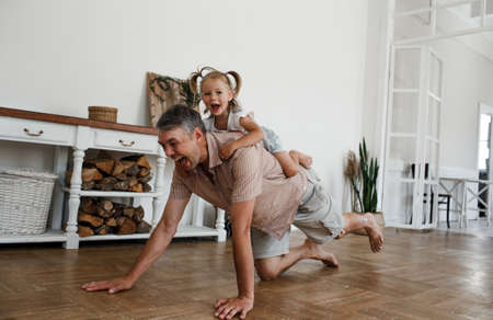 a little girl and her dad having fun together, a child rides on his father's back and hugs himの写真素材
