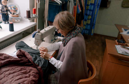 A female dressmaker uses a sewing machine to create custom-made clothes in a workshop. A female seamstress is busy sewing clothes in the workplace.の写真素材