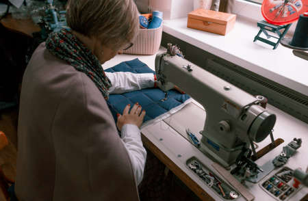 A female dressmaker uses a sewing machine to create custom-made clothes in a workshop. A female seamstress is busy sewing clothes in the workplace.の写真素材