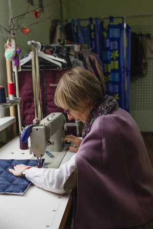 A female dressmaker uses a sewing machine to create custom-made clothes in a workshop. A female...