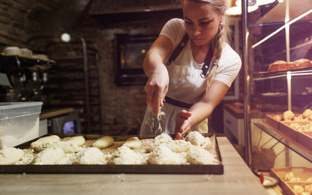 a girl cook in a cafe sprinkles coconut shavings on raw pies lying on a tray.