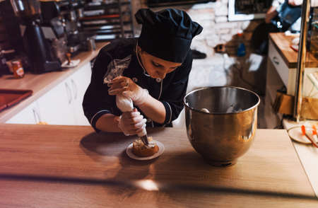 a pastry chef girl decorates a shortbread cake with a pastry bag with protein cream, squeezes out the cream. Close-upの写真素材