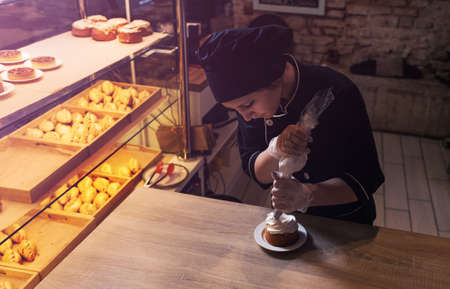 a pastry chef girl decorates a shortbread cake with a pastry bag with protein cream, squeezes out the cream. Close-upの写真素材