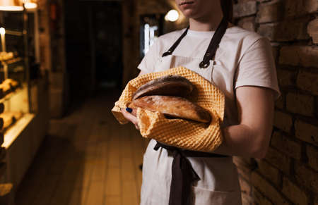 The concept of homemade bread, a small bakery, natural farm products, domestic production. Healthy and delicious organic food. A woman holds a freshly baked dark round bread in her hands.の写真素材
