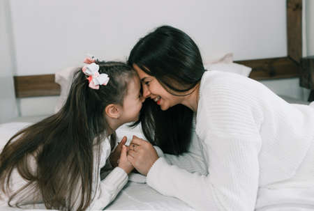 a young mother spends time with her daughter in bed, lying opposite each other, pressing her head.の写真素材