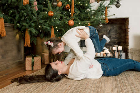 a happy mother lifts her daughter in her arms while lying under a Christmas tree. happy familyの写真素材